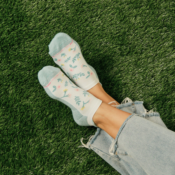 Ankle compression socks with a floral pattern, featuring a light blue and white design, worn with distressed jeans on grass.