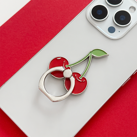 Silver phone with a Coconut Lane cherry-patterned adhesive ring on a red and white background.