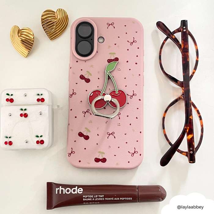 Pink phone in cherry-patterned case, tortoiseshell glasses, gold heart hair clips, cherry earrings, and phone ring.