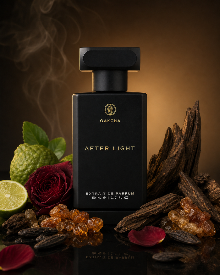 Front view of After Light perfume bottle showing matte black rectangular bottle with gold logo among rose petals, lime, resin, and wood on a dark backdrop