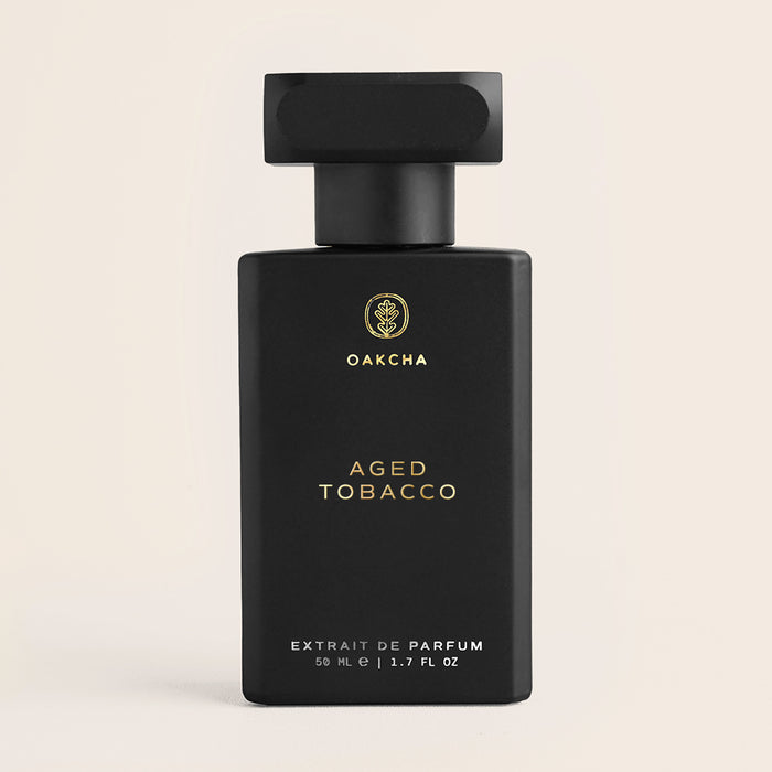 Front view of Aged Tobacco perfume, matte black rectangular bottle with gold logo and square black cap on beige background