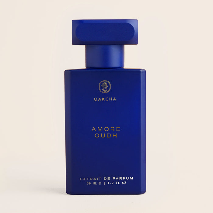 Front view of Amore Oudh 50 ml perfume bottle showcasing a matte cobalt-blue rectangular bottle with gold lettering on a beige background