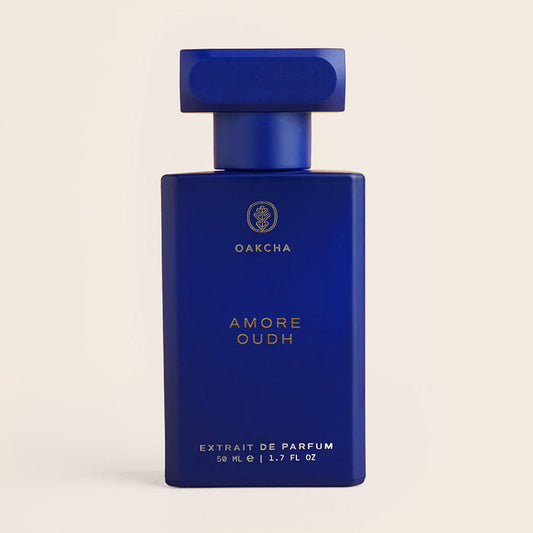 Front view of Amore Oudh 50 ml perfume bottle showcasing a matte cobalt-blue rectangular bottle with gold lettering on a beige background