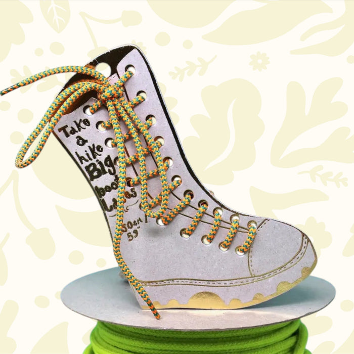 Ark Big Boot Laces in orange and green rest on vibrant laces spool, blue sky and clouds making a bright, eye-catching backdrop.