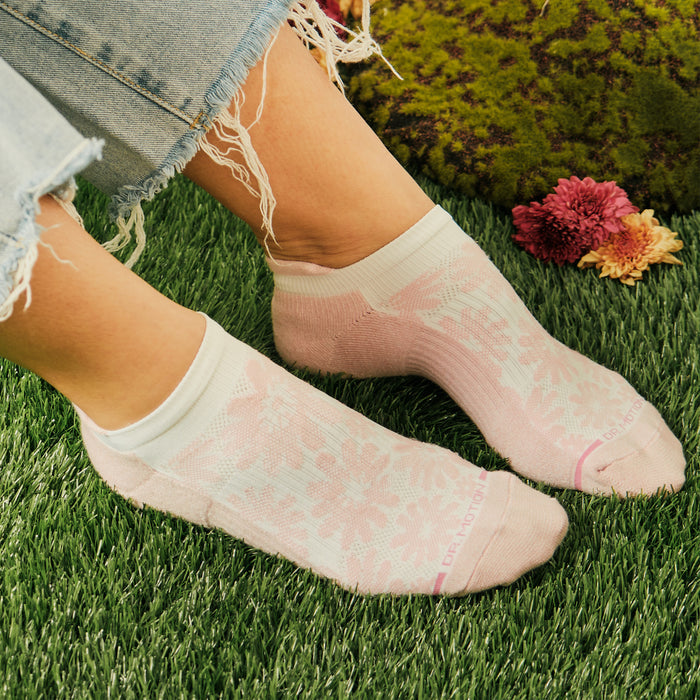 Ankle compression socks with a floral pattern in pink and white, worn with frayed denim on grass.