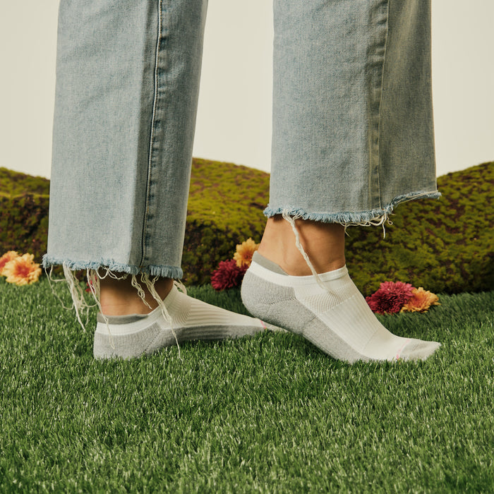 Ankle compression socks with a floral design, worn with frayed denim jeans on a grassy surface.