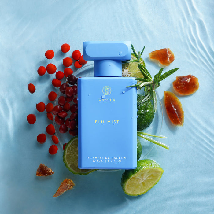 Front view of Blu Mist perfume bottle showcasing sky-blue rectangular bottle with fruit accents on light blue fabric background