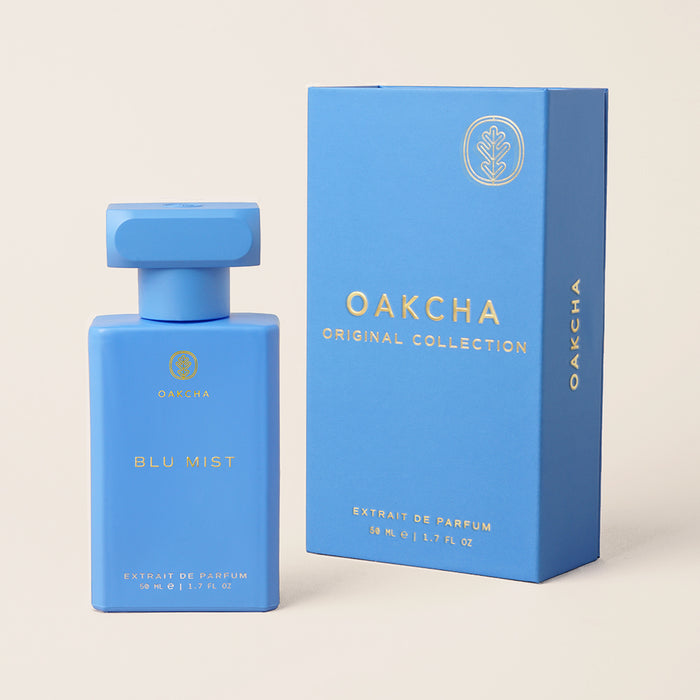 Front view of Blu Mist perfume bottle and matching blue box showing gold logo on a light beige background