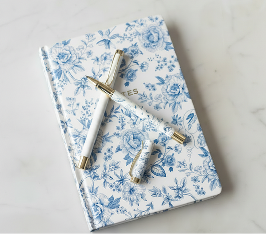 Matching set of a blue and white floral notebook, a blue and white floral pen, and a pink and white striped pen.