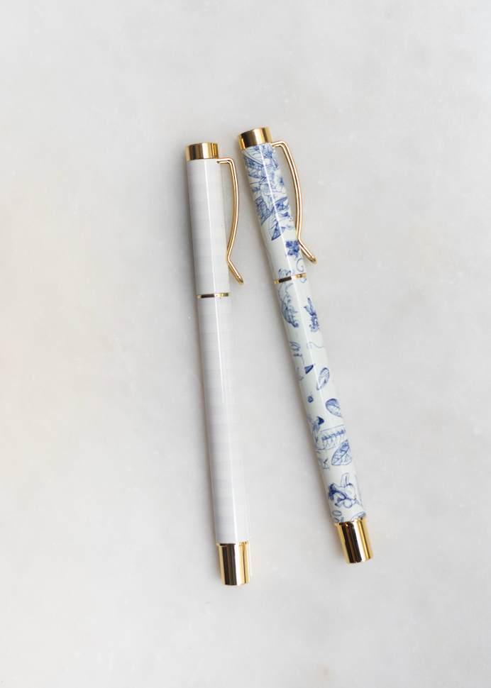 Two pens with gold details, one with a blue and white floral pattern, and one with pink and white strips.