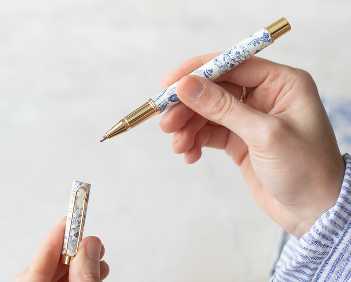 Hand holding a blue and white floral pattern pen with gold details.
