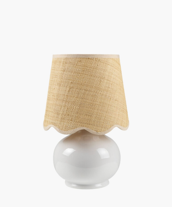 A white ceramic table lamp has a textured natural fiber shade with wavy edges. The design is simple and rustic, conveying a cozy feel. | Wildwood Home Co.