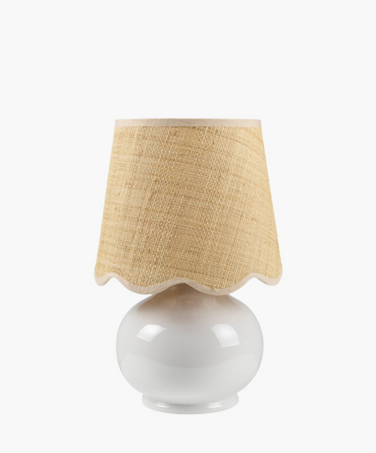 A white ceramic table lamp has a textured natural fiber shade with wavy edges. The design is simple and rustic, conveying a cozy feel. | Wildwood Home Co.