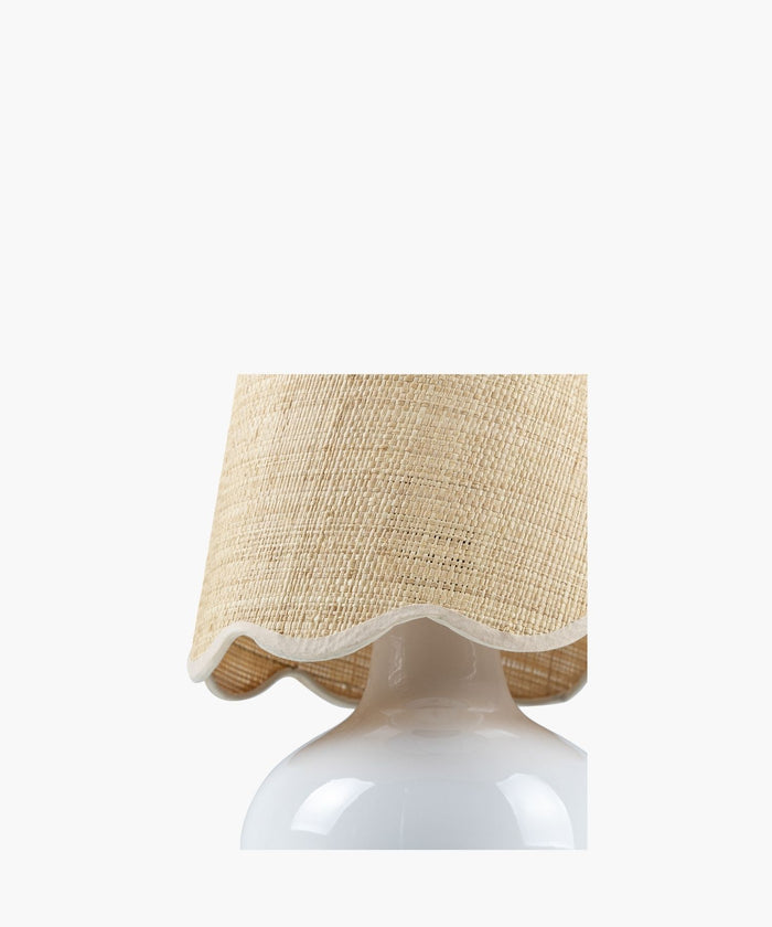 A white ceramic table lamp has a textured natural fiber shade with wavy edges. The design is simple and rustic, conveying a cozy feel. | Wildwood Home Co.