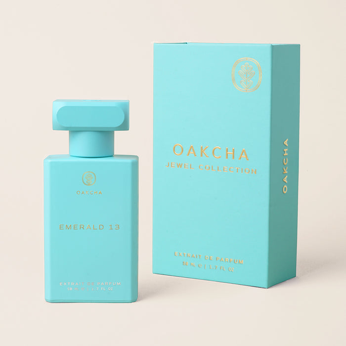 Front view of Emerald 13 perfume bottle and matching turquoise box with matte finish and gold foil logo on beige background