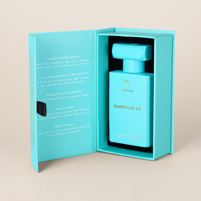 Front view of Emerald 13 50ml perfume bottle inside open turquoise presentation box showcasing rectangular bottle with square cap on beige background