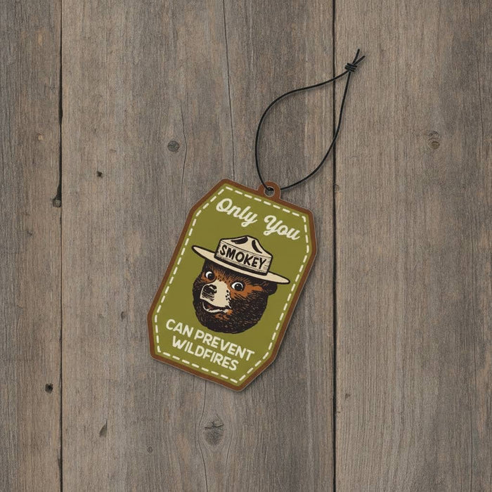 Forager Provisions LTD Smokey Bear hanging air freshener with cypress and fir scent on a rustic wooden background.
