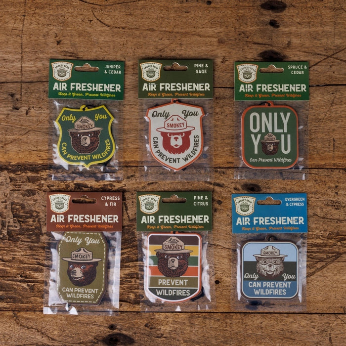 Six Good & Well Supply Co Spruce & Cedar Smokey Bear Air Fresheners, sealed and displayed on a wooden surface for freshness.