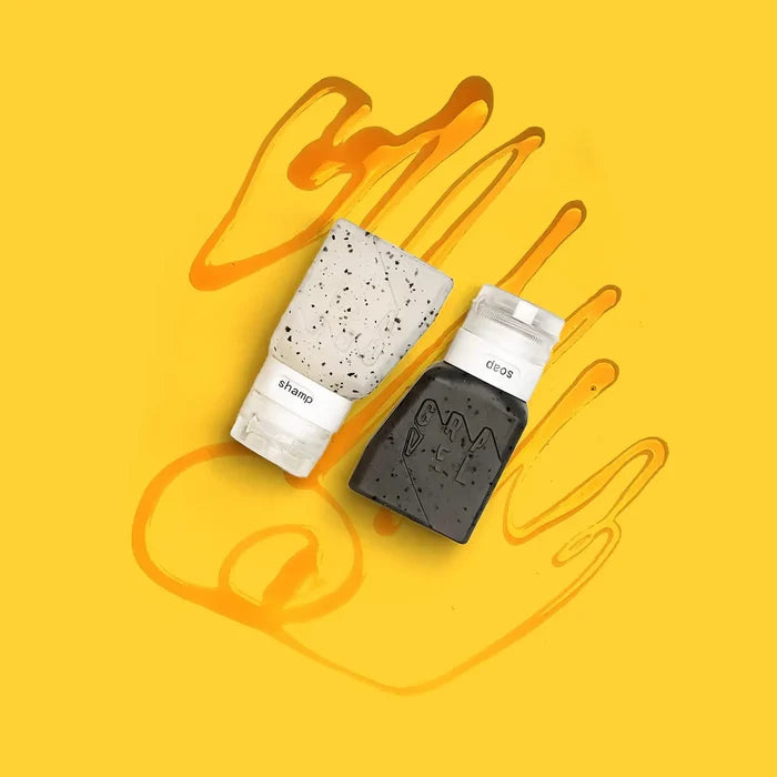 Gravel Outdoor Travel Bottles 3oz, grey & clear, two-pack on yellow background with orange hand outline. Leak-proof TSA-approved.