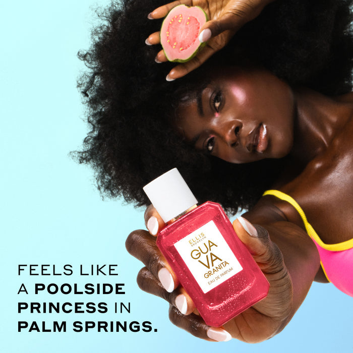 Woman with brown hair wearing a pink and yellow bikini top holds GUAVA GRANITA Eau de Parfum 50ml covered in water droplets out in front of her in one hand and a slice of guava in her other hand next to her head against a blue background with black text that reads "Feels like a poolside princess in Palm Springs.