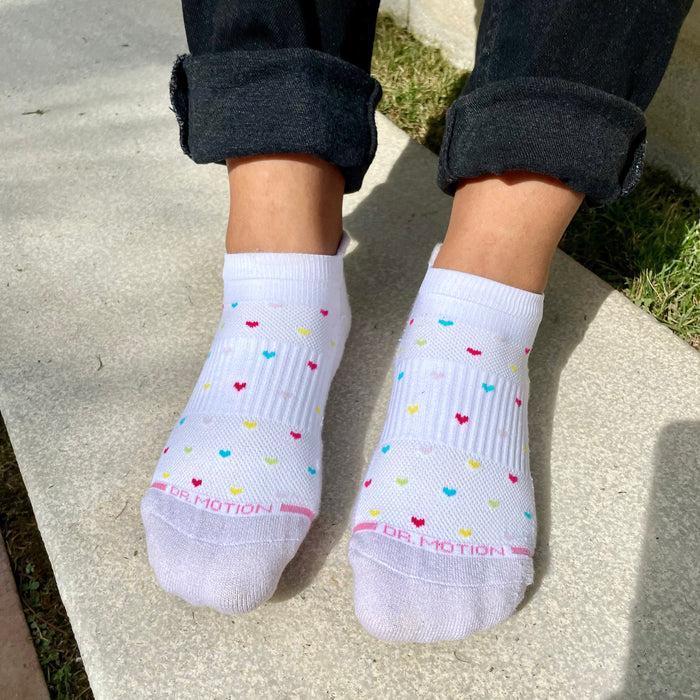 White ankle compression socks with colorful heart patterns, worn with rolled black jeans.