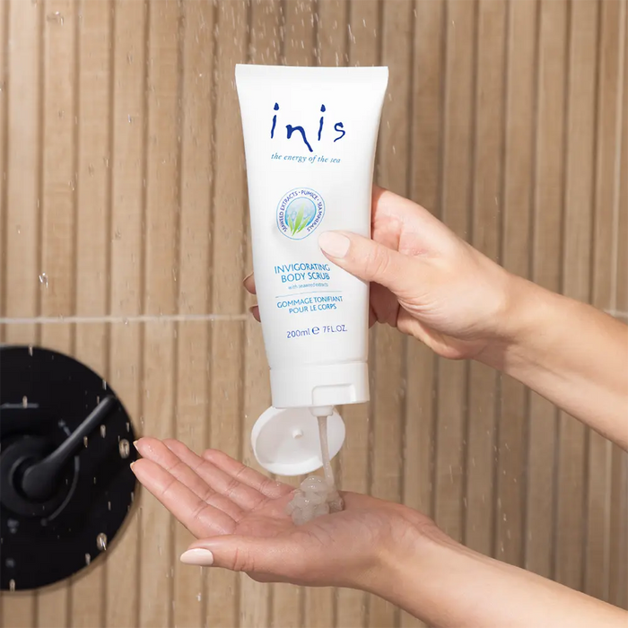 Hand holding a tube of 'inis' body scrub with the running water background