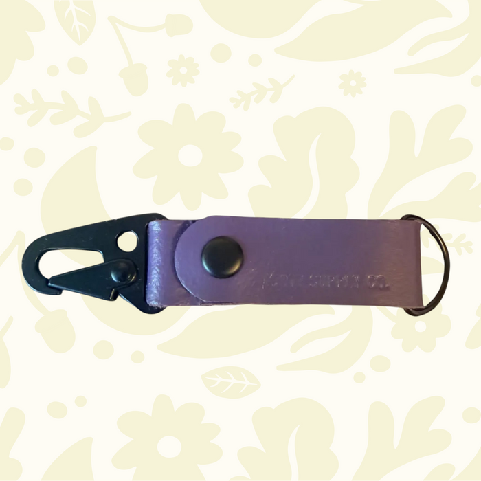 Purple Kjøtt Forager Provisions Leather Key Fob with snap, clip, keyring on a floral background. Stylish accessory.