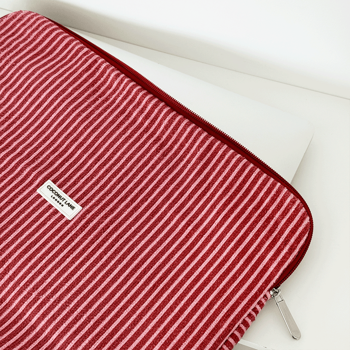White laptop in a striped Mulberry TOWEL laptop sleeve with pink and beige accents on a white surface.