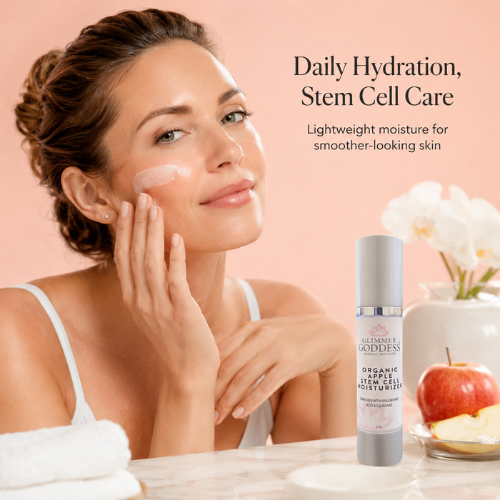 Ultra-realistic lifestyle image of Glimmer Goddess® Organic Apple Stem Cell Moisturizer in a white airless pump bottle with silver accents beside a woman applying moisturizer during her skincare routine, highlighting lightweight hydration, apple stem cell care, hyaluronic acid, squalane, and smoother-looking skin.