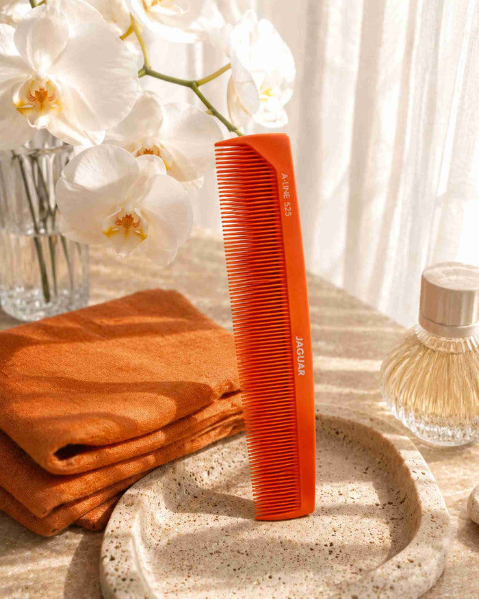 Orange fine-tooth comb standing near towels on a countertop