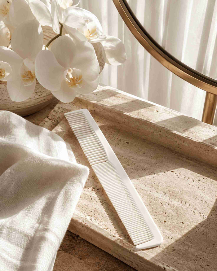 White hair sectioning comb lying on white fabric beside vanity mirror