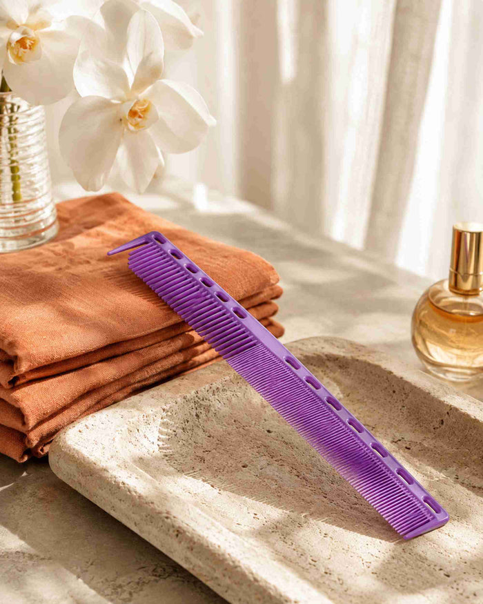 Purple sectioning hair comb resting on a stone surface beside folded towels
