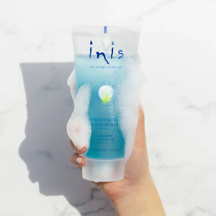 Hand holding a tube of 'inis' shower gel with a marble background