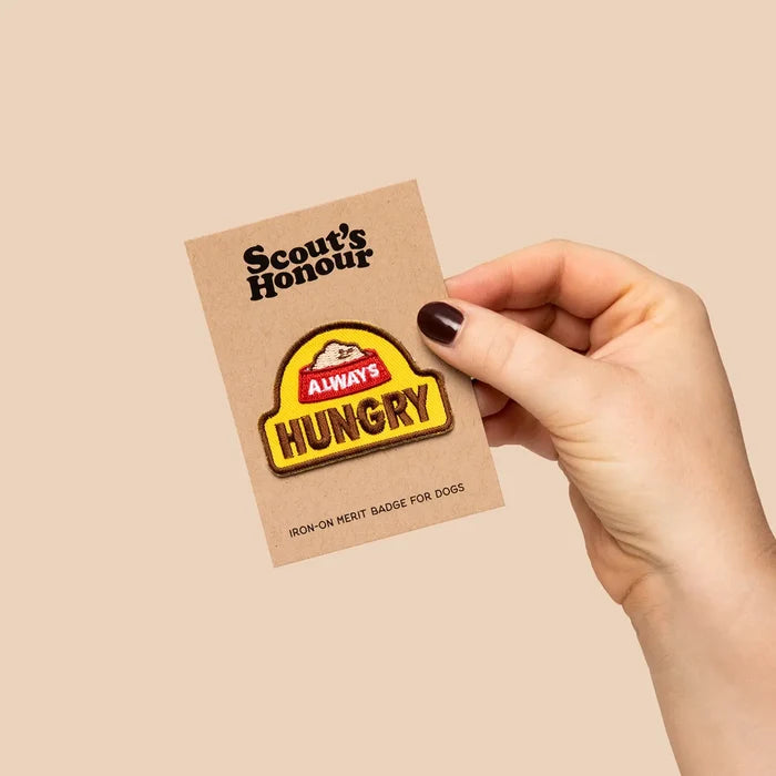 Hand holds Scout’s Honour Always Hungry Dog Patch—perfect badge for snack-loving dogs and pet parents; food treat accessory.