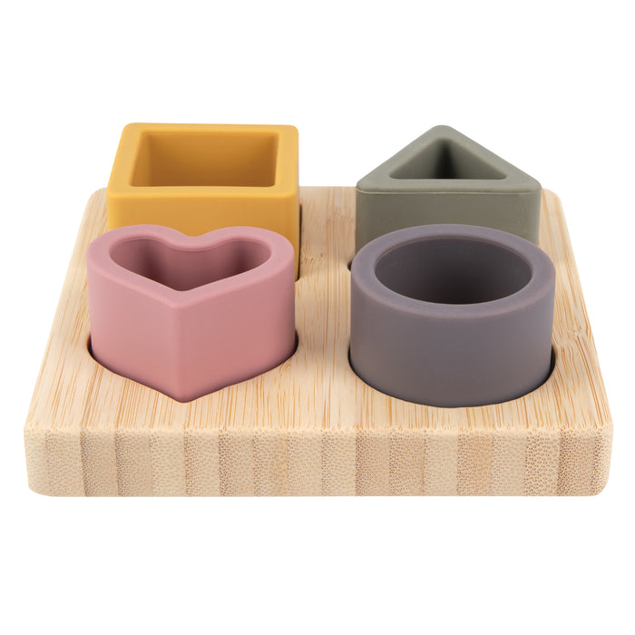 The Silicone Puzzle Toy is a wooden board puzzle for cognitive development with four removable silicone shapes—a yellow square, green triangle, pink heart, and gray circle—that fit into matching cut-outs to build hand-eye coordination.