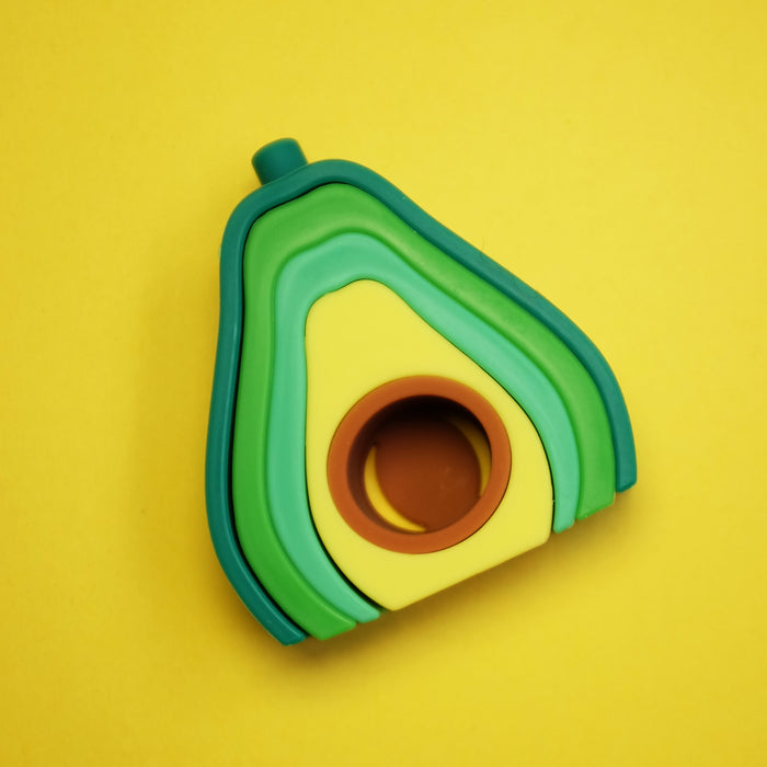 The Silicone Stacking Avocado Toy features four stackable, nestable avocado-shaped pieces in green and yellow, designed to promote hand-eye coordination and cognitive skills. The smallest piece includes a brown pit-like circle at its center.