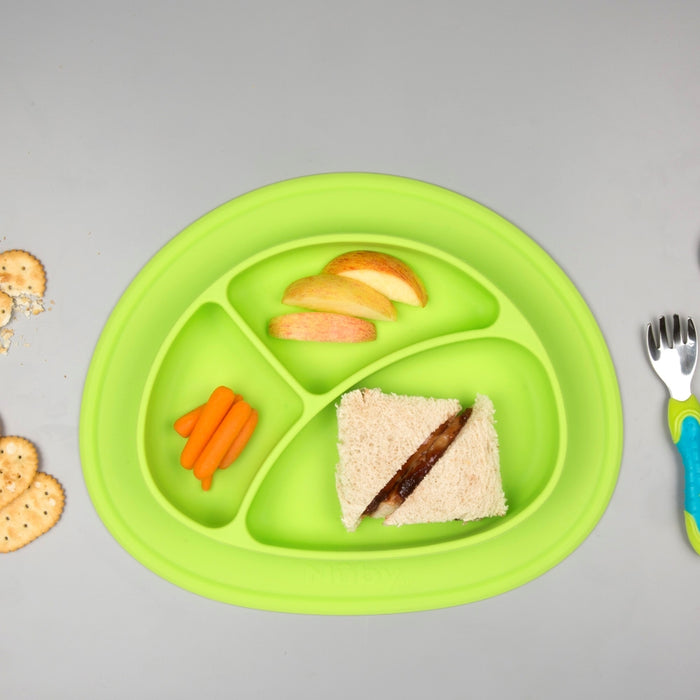 A Sure Grip Miracle Mat 3-Section Plate in green holds apple slices, baby carrots, and a triangle PB&J sandwich. Crackers and baby utensils—a fork and spoon—rest on the gray tabletop beside the plate.