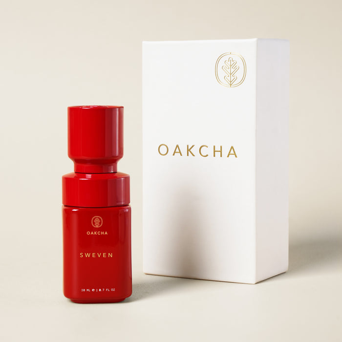 Front view of Sweven perfume oil bottle in red showing gold Oakcha logo, beside white Oakcha box on light beige background