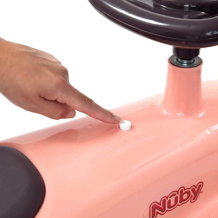 A hand presses a white button on the pink Twist N' Ride Classic Car, with part of the black steering wheel visible at the top.