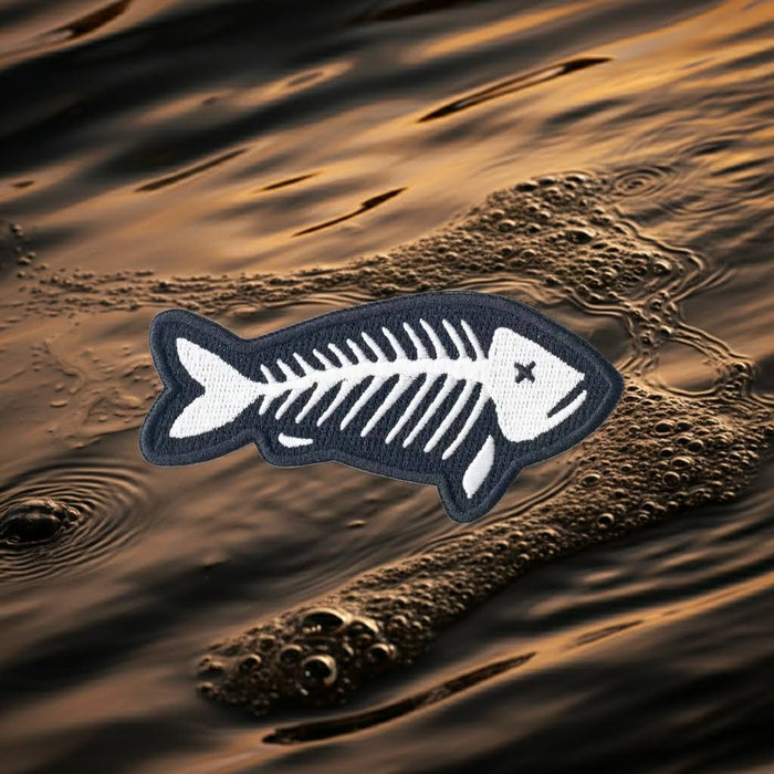 Forager Provisions LTD embroidered fish skeleton patch with white stitching on a dark background over rippling water.