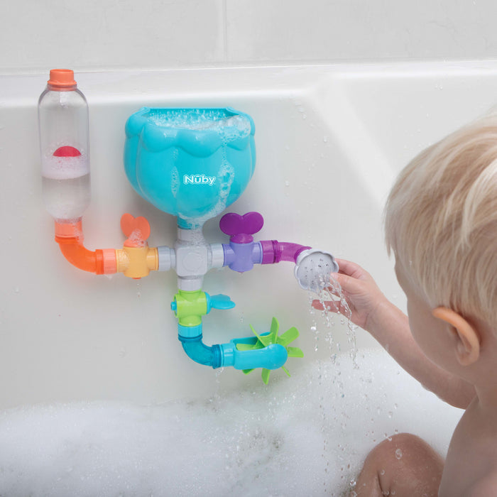 A toddler in a bathtub enjoys water play with Nuby's Wacky Waterworks, a colorful bath toy attached to the tub wall; as water flows through pipes and spinning wheels, it encourages cognitive development.
